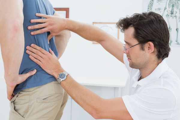 Side view close-up of a male physiotherapist examining mans back